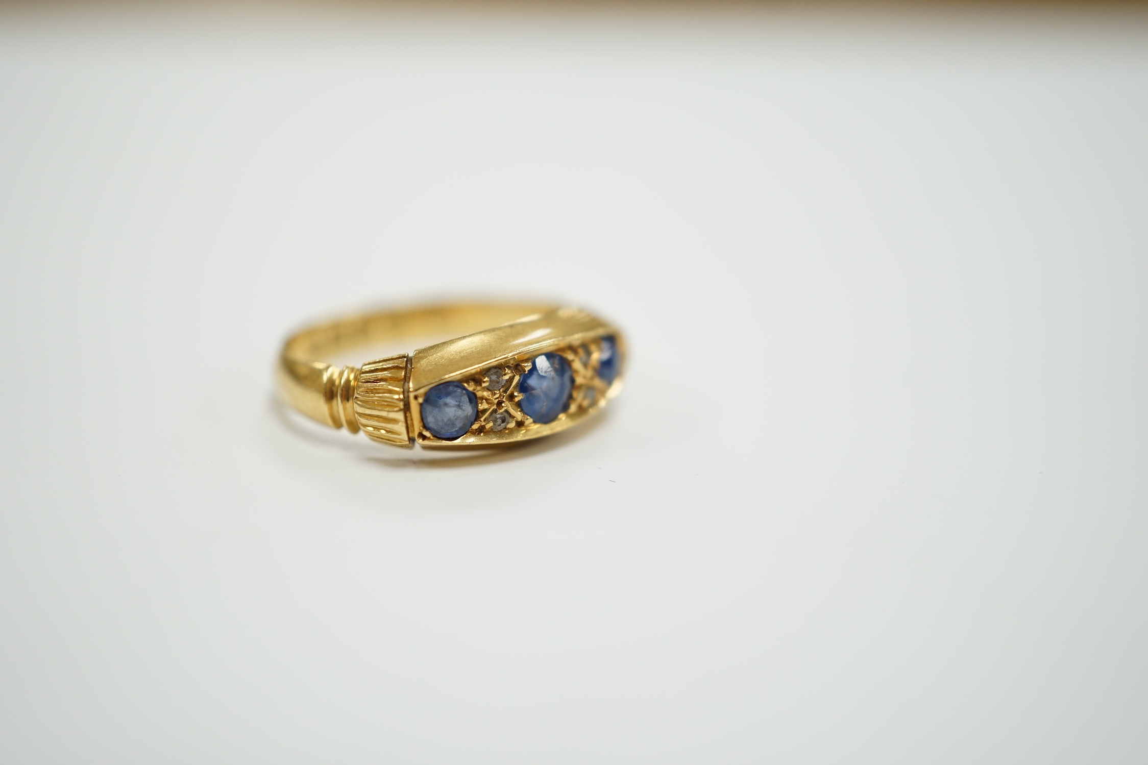 A George V 18ct gold and three stone sapphire set ring, with diamond chip spacers, size K, gross weight 3.3 grams.